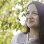 Eine Frau lächelt vor einem blätterhintergrund in die Ferne